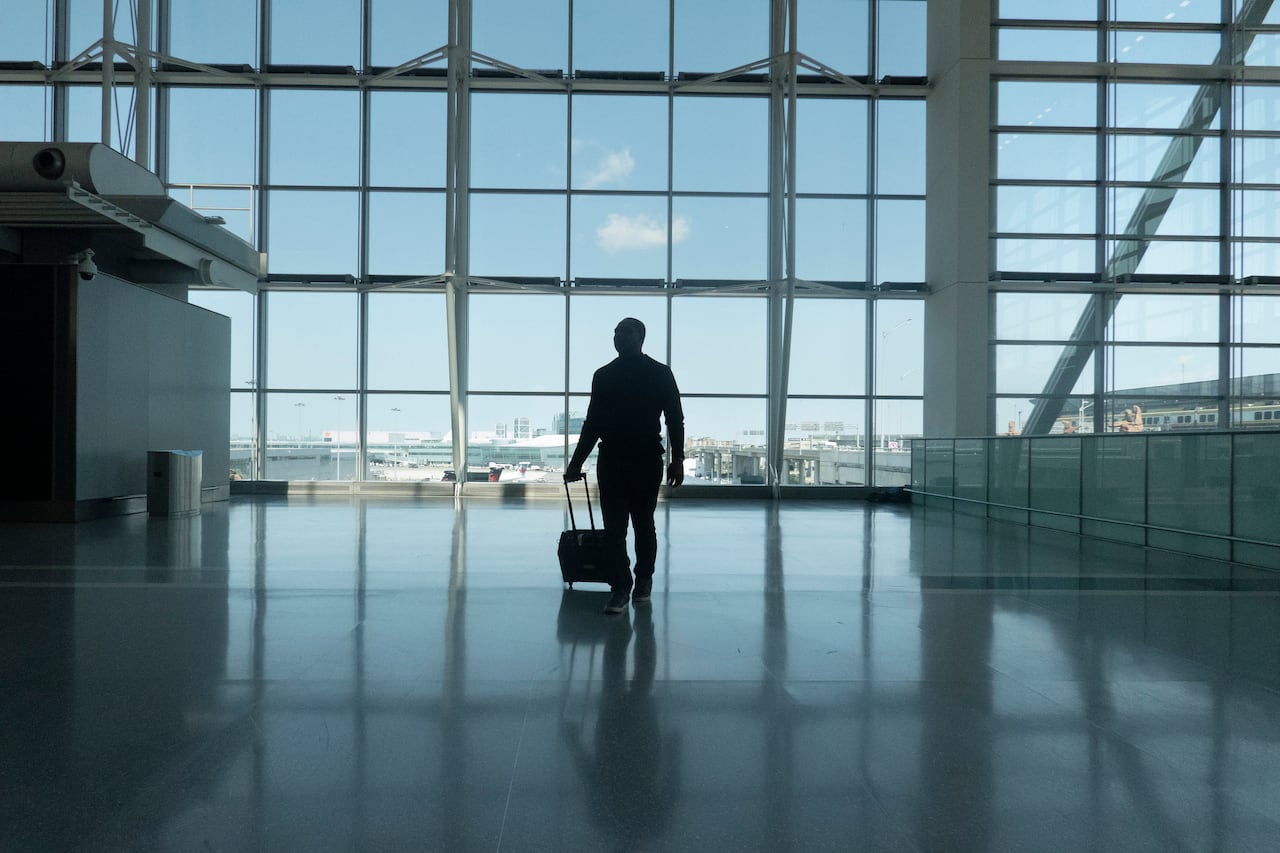 A man walks through an airport terminal with a bag.