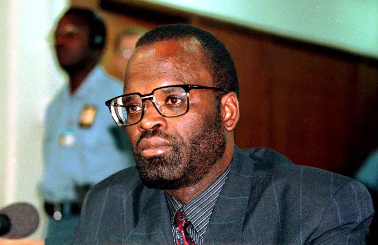 A man sits in at a microphone, in a courtroom.