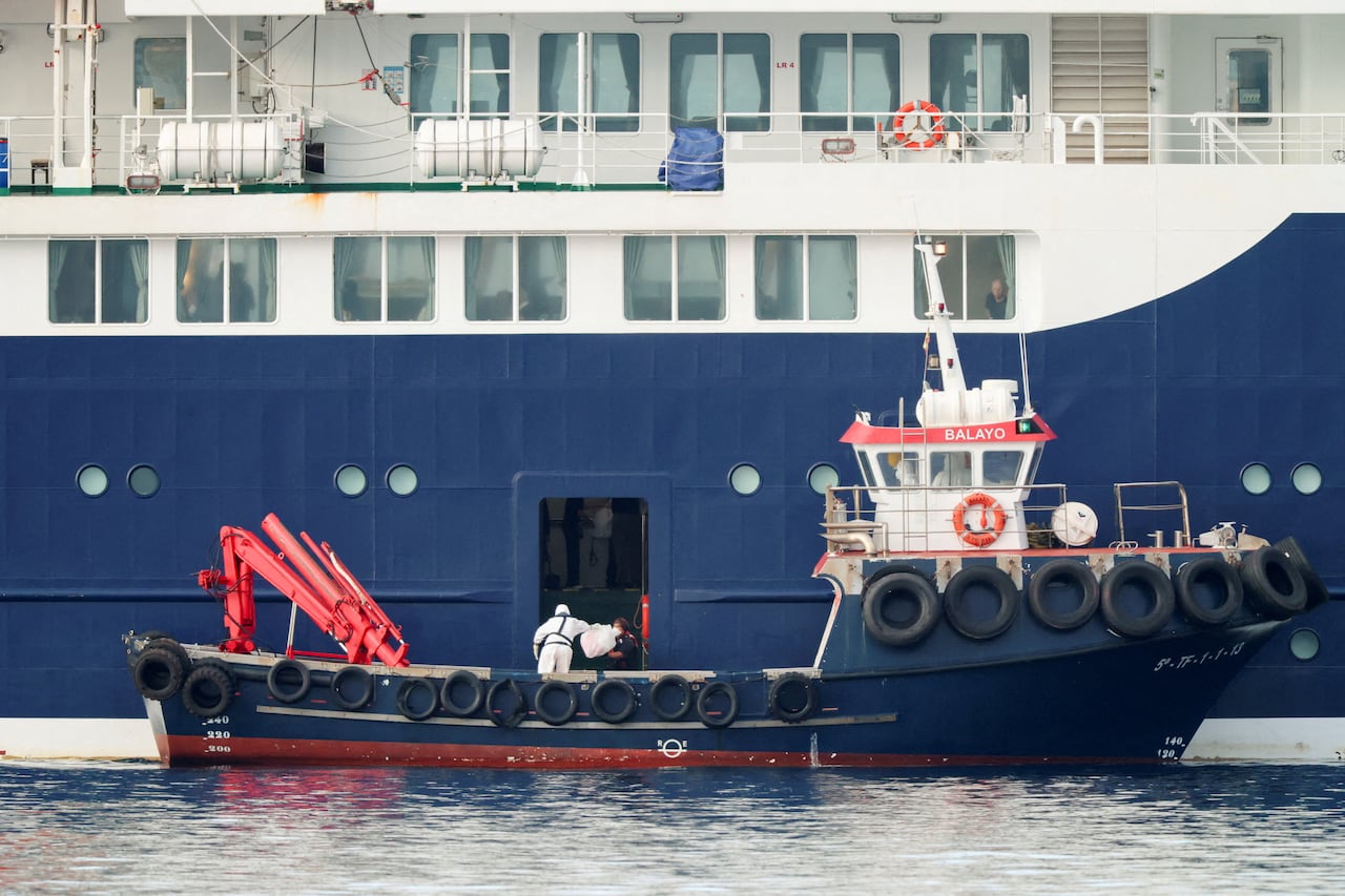 A person wearing personal protective equipment (PPE) on a boat transfers a package to the cruise ship MV Hondius.
