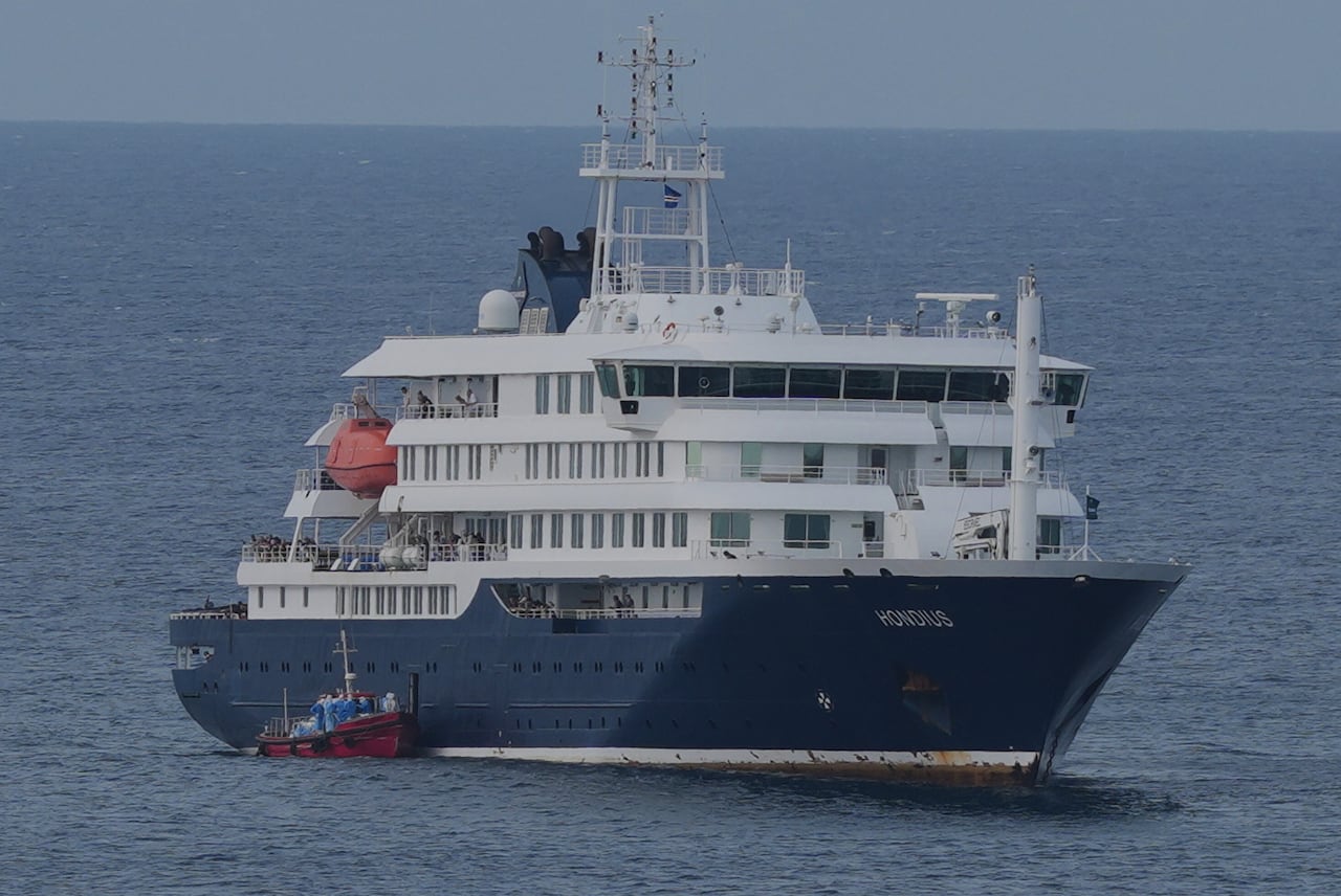 A skiff with people wearing blue protective clothing docks with a larger ship.