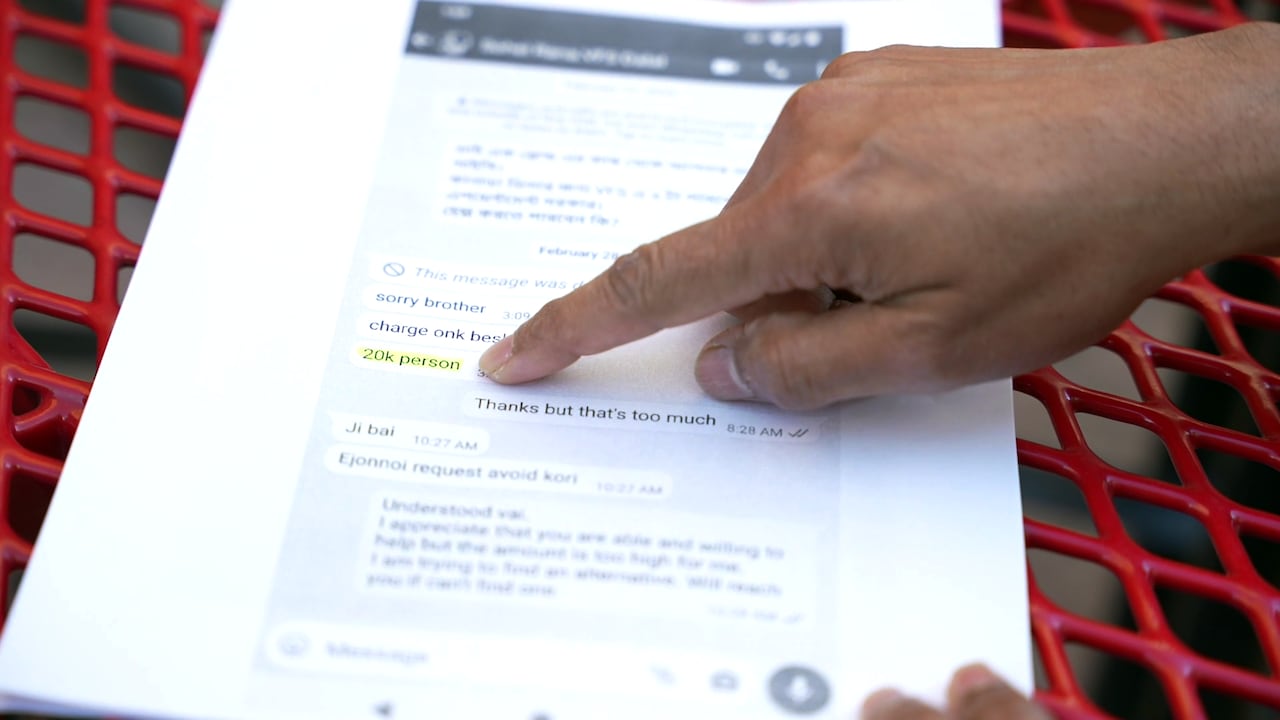 A man points to a paper with a screenshot of a chat with a middleman, that quotes $20,000 Bangladeshi takas per person (or about $250 Canadian at the time in 2024), to get an appointment at a visa application centre.