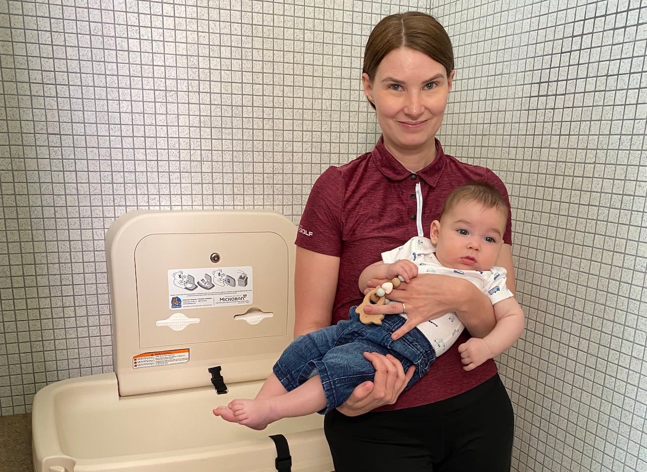 A woman holds a baby inside a bathroom