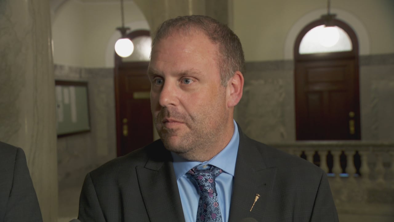 A man is pictured wearing a shirt and tie in a hallway.