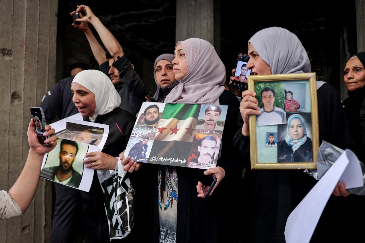 Residents gather in a street holding up photos of people.