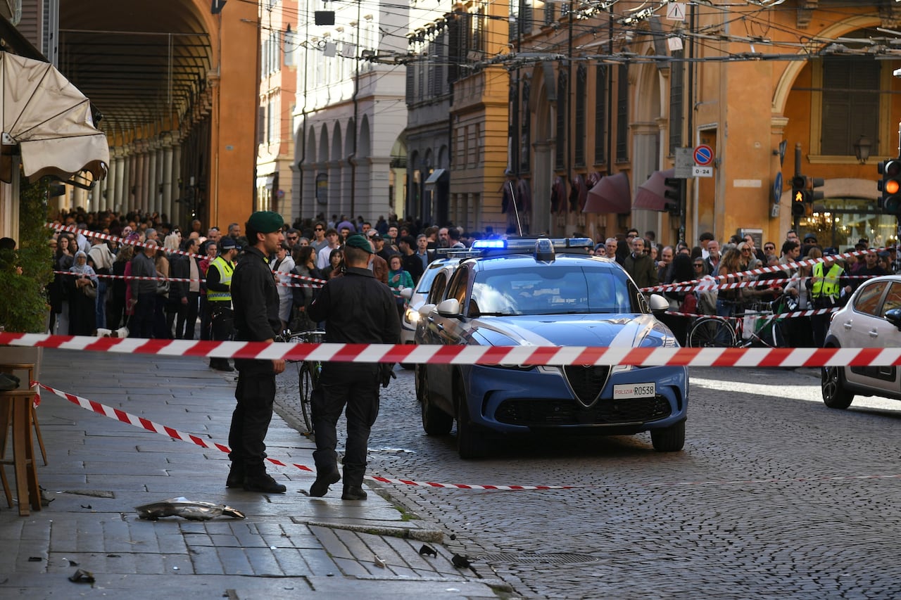 Police patrol the scene of a car collision while a large crowd looks on.