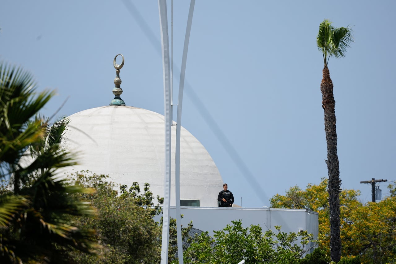 An armed police officer stands guard on the balcony of a mosque.