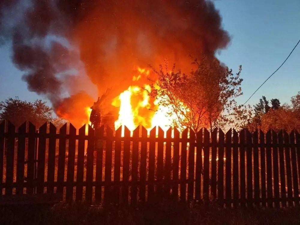 A house is seen engulfed in flames behind a wooden picket fence.