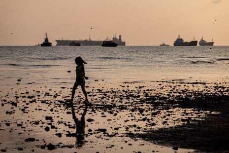A child plays on the shore as an oil tanker sails in the background