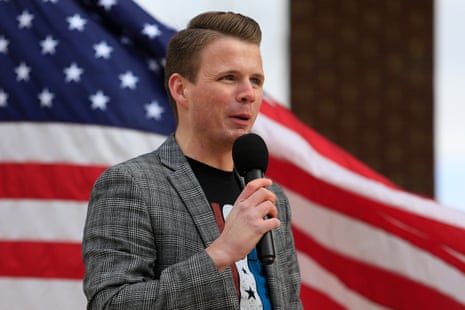 A man speaking into a microphone with a US flag flying in the background.